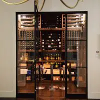 The finished doorway to the residential custom wine room in Dallas. Iron door flanked by glass window panes open up into the new wine room.